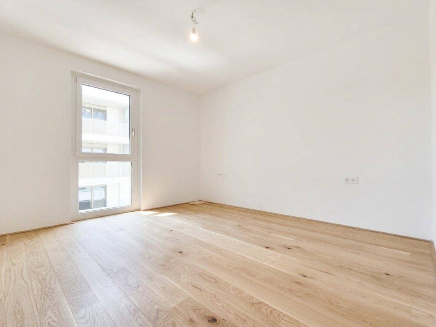 Helles Schlafzimmer mit Eichenparkett und großem Fenster, bereit zur Einrichtung.