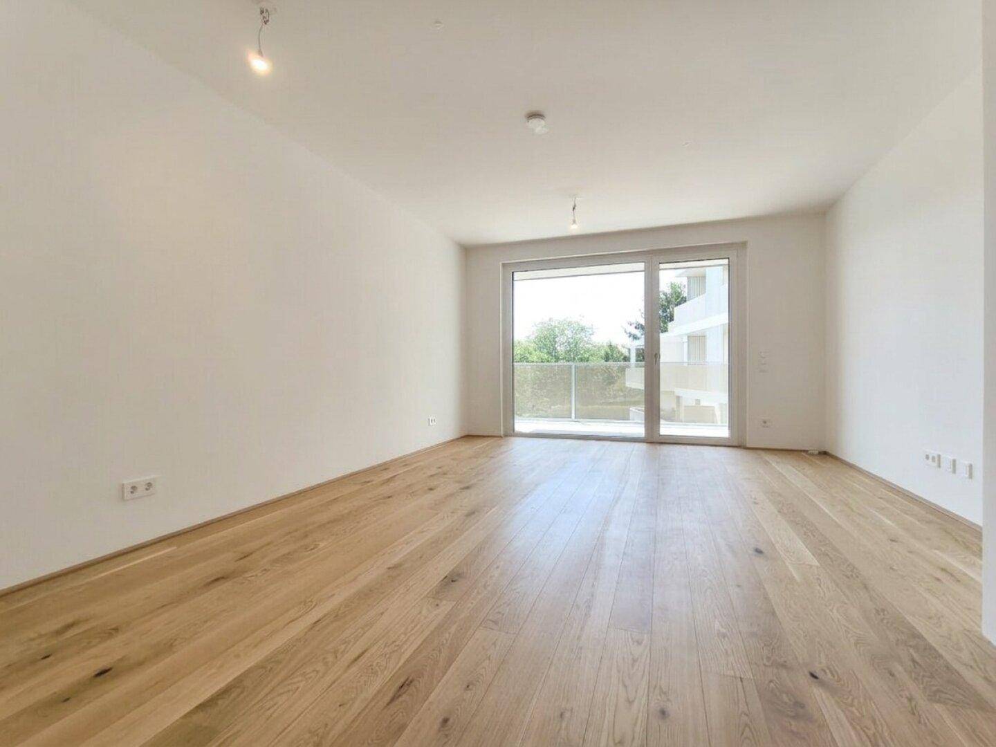 Geräumiger, heller Raum mit Holzboden und Zugang zu einem Außenbereich.
