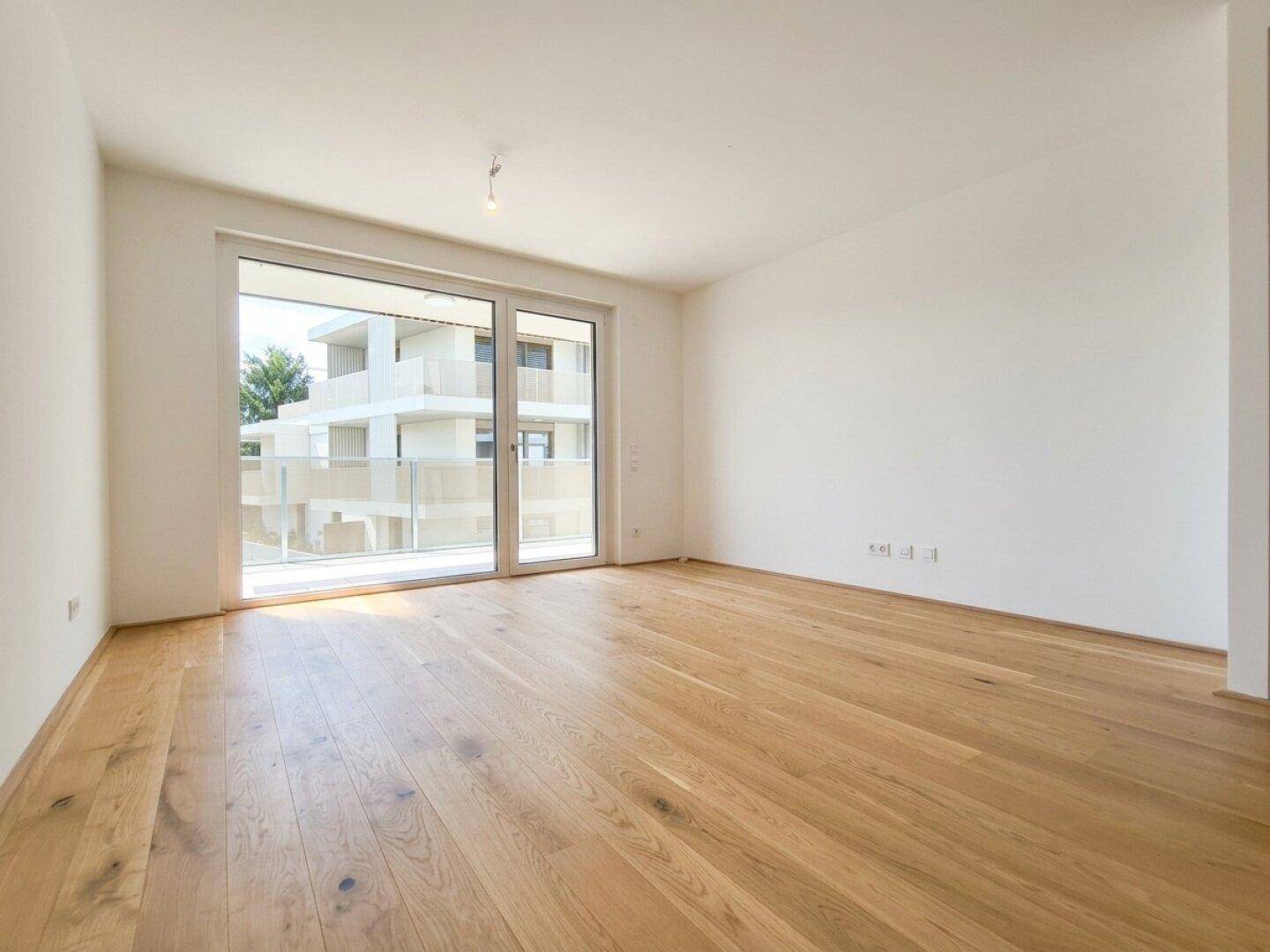Heller, leerer Raum mit Eichenparkett und großer Schiebetür zu einem Balkon.