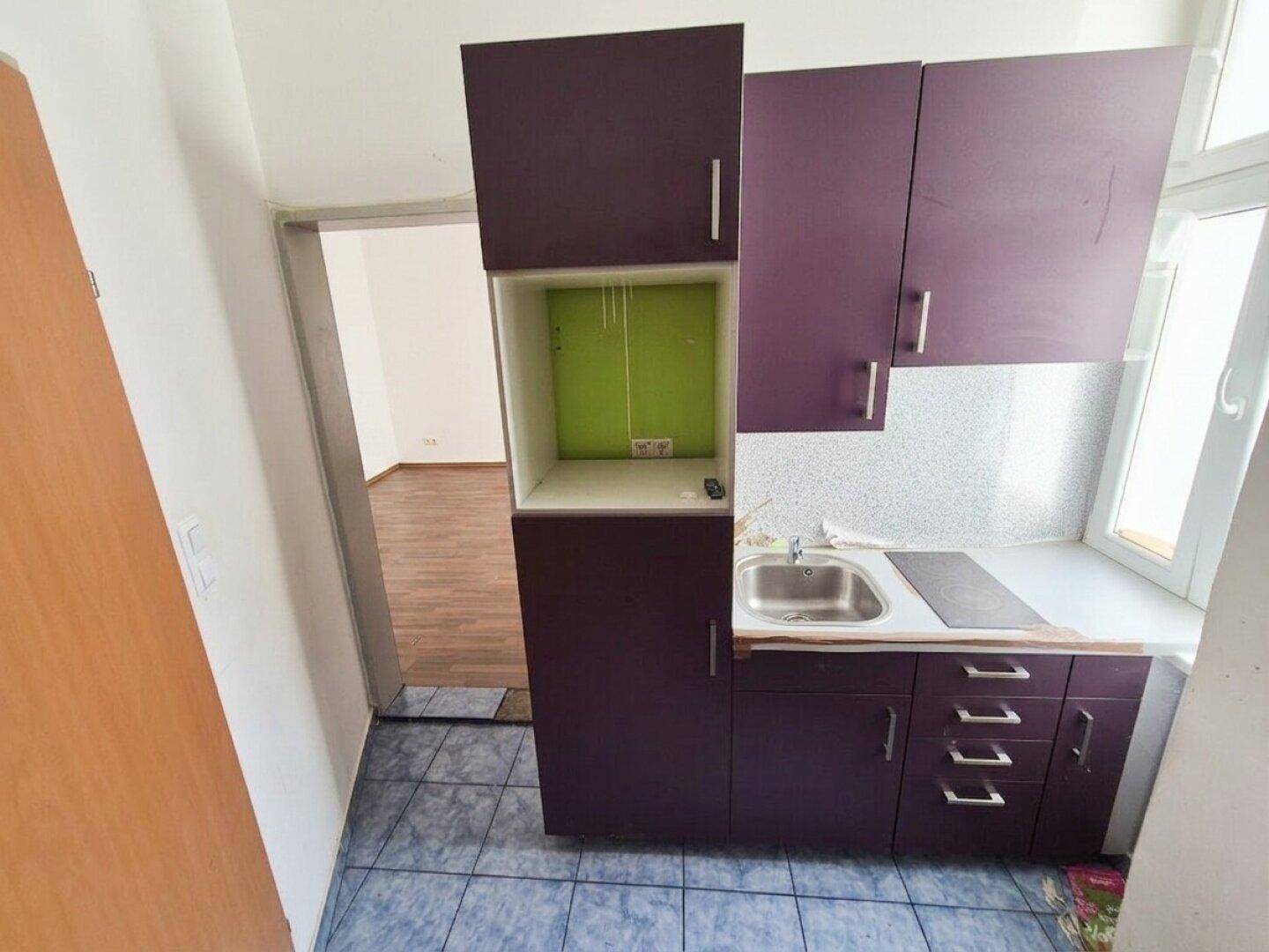 Kleine Küchenzeile mit lila Schränken, Spüle und Kochfeld, ideal für kompaktes Wohnen.