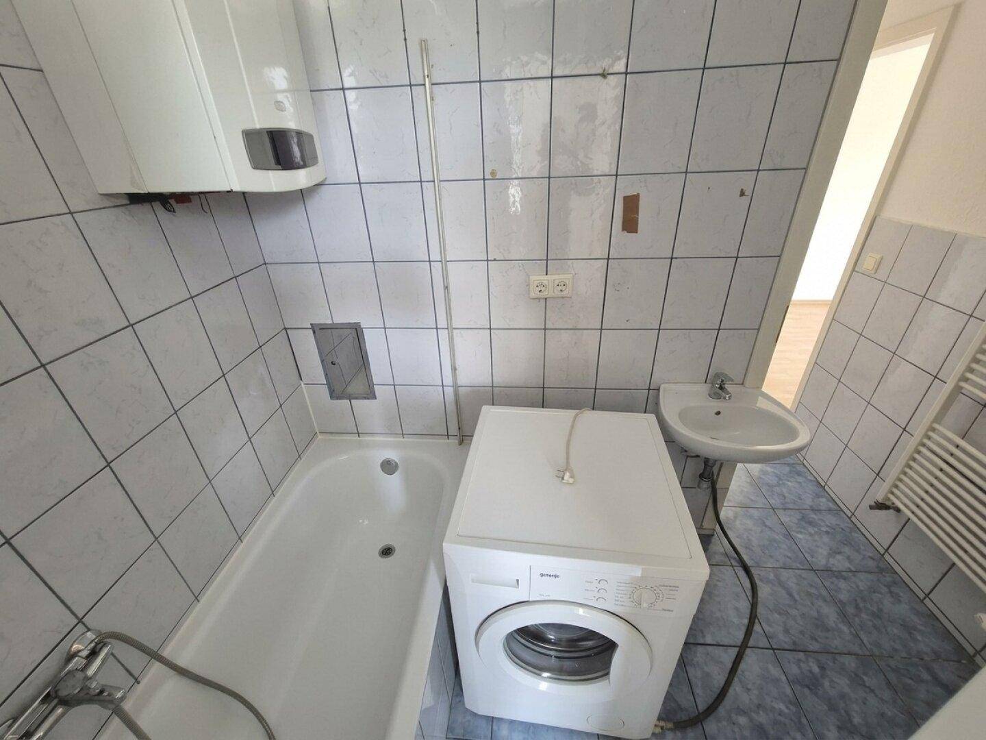 Badezimmer mit Badewanne, Waschbecken, Waschmaschine und Wandfliesen in hellem Blau und Weiß.