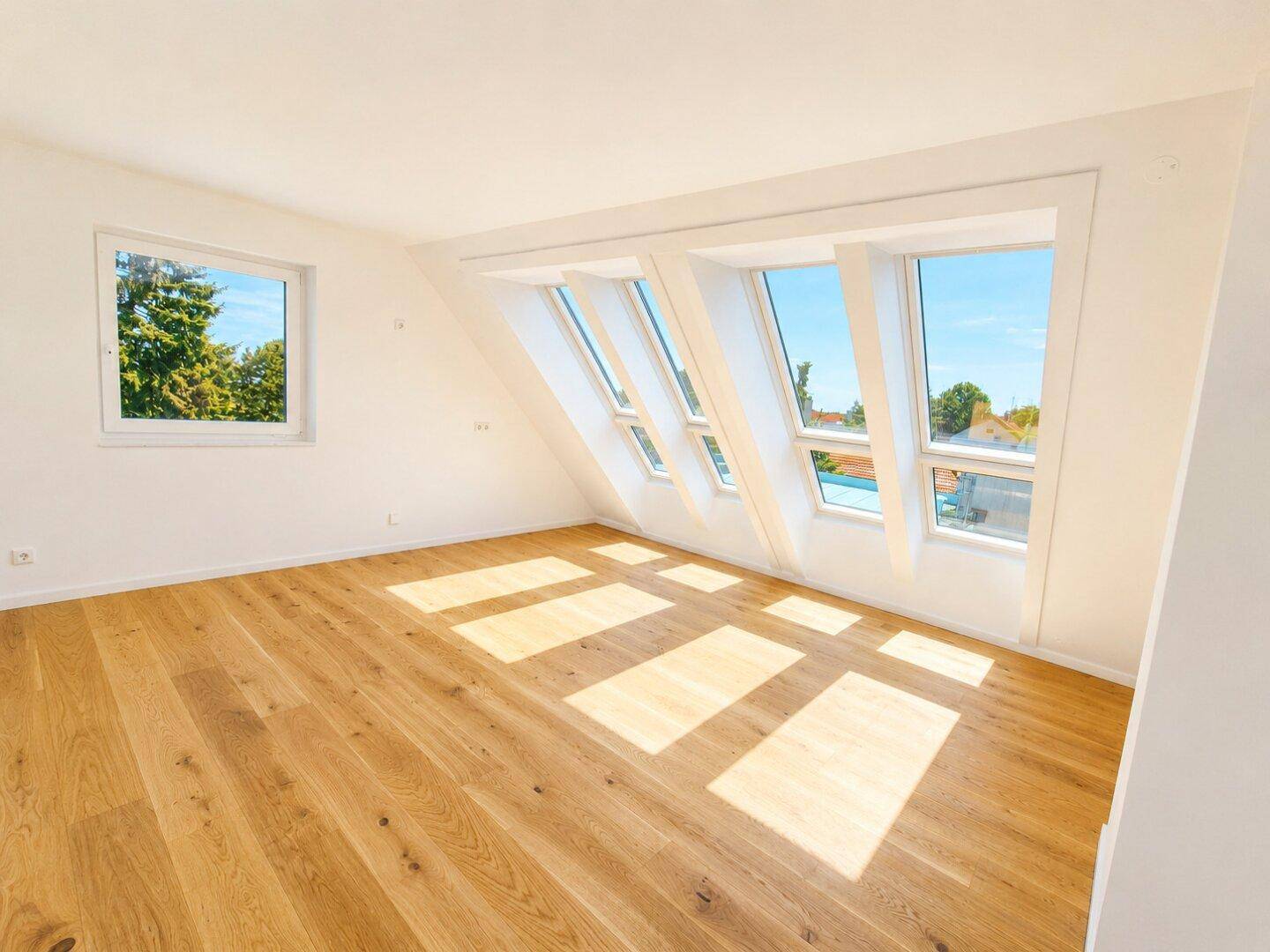 Lichtdurchfluteter Dachgeschossraum mit Holzboden und mehreren Dachfenstern, bietet viel Tageslicht.