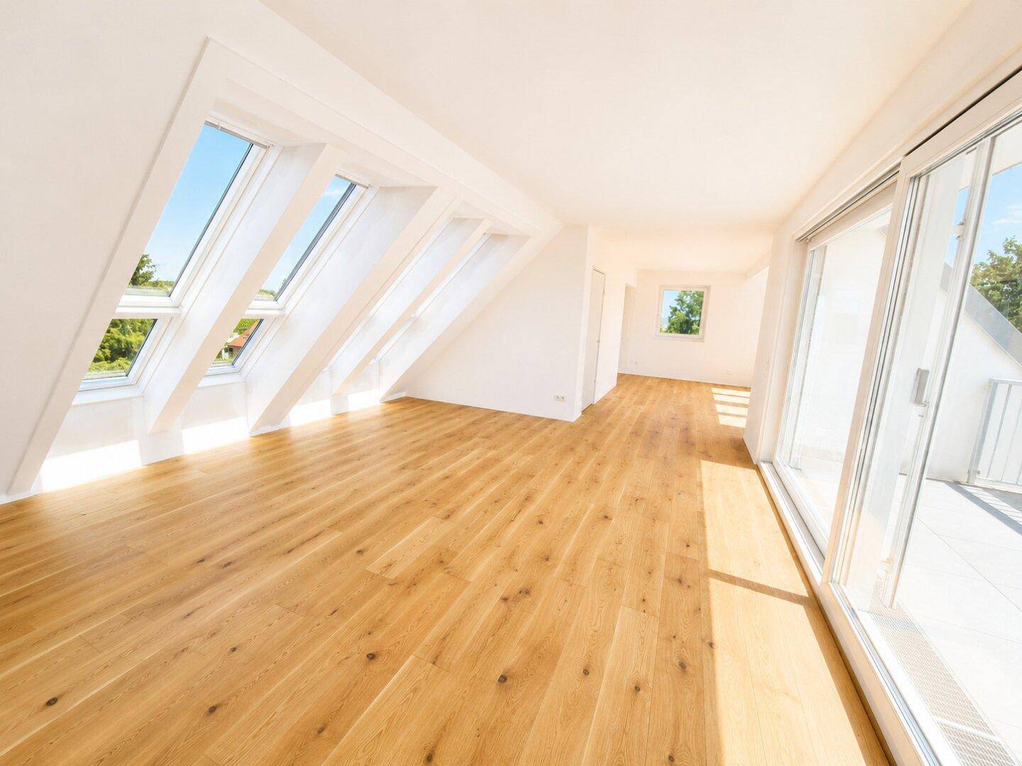 Heller Dachgeschossraum mit Holzdielenboden, großen Dachfenstern und Zugang zu einem Balkon.
