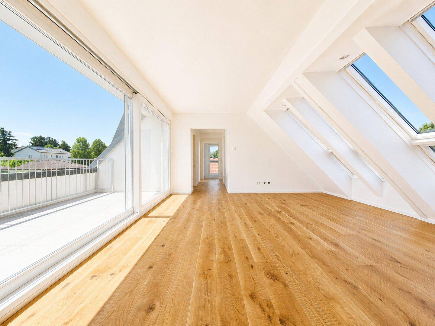 Geräumiger, heller Dachgeschossraum mit Holzdielenboden, Dachfenstern und Balkonzugang.
