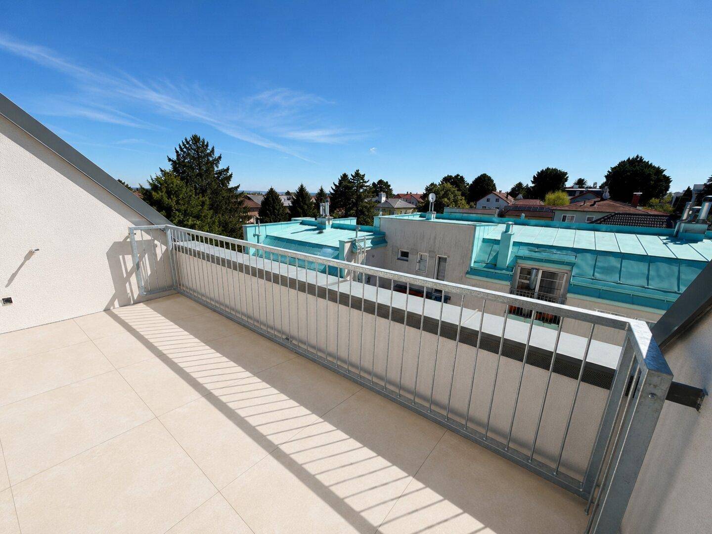 Geräumiger Balkon mit Fliesenboden und Metallgeländer, bietet einen weiten Blick über die Dächer der Umgebung.