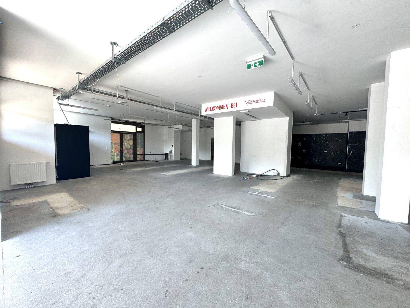 Großer, offener Ladenbereich mit Betonboden, hohen Decken und sichtbaren Deckeninstallationen.