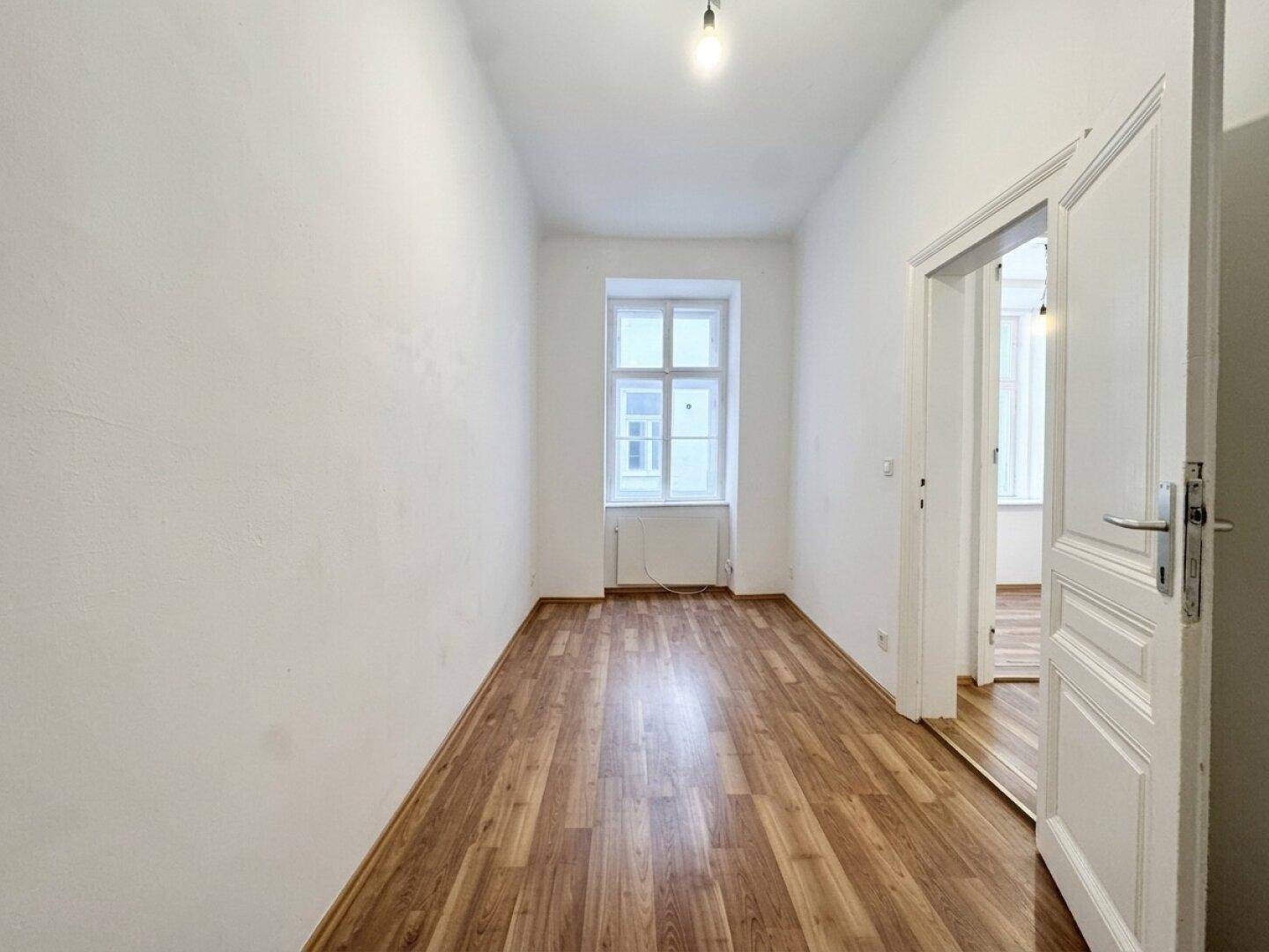 Leerer Raum mit Laminatboden und Fenster, vielseitig nutzbar als Schlaf- oder Arbeitszimmer.