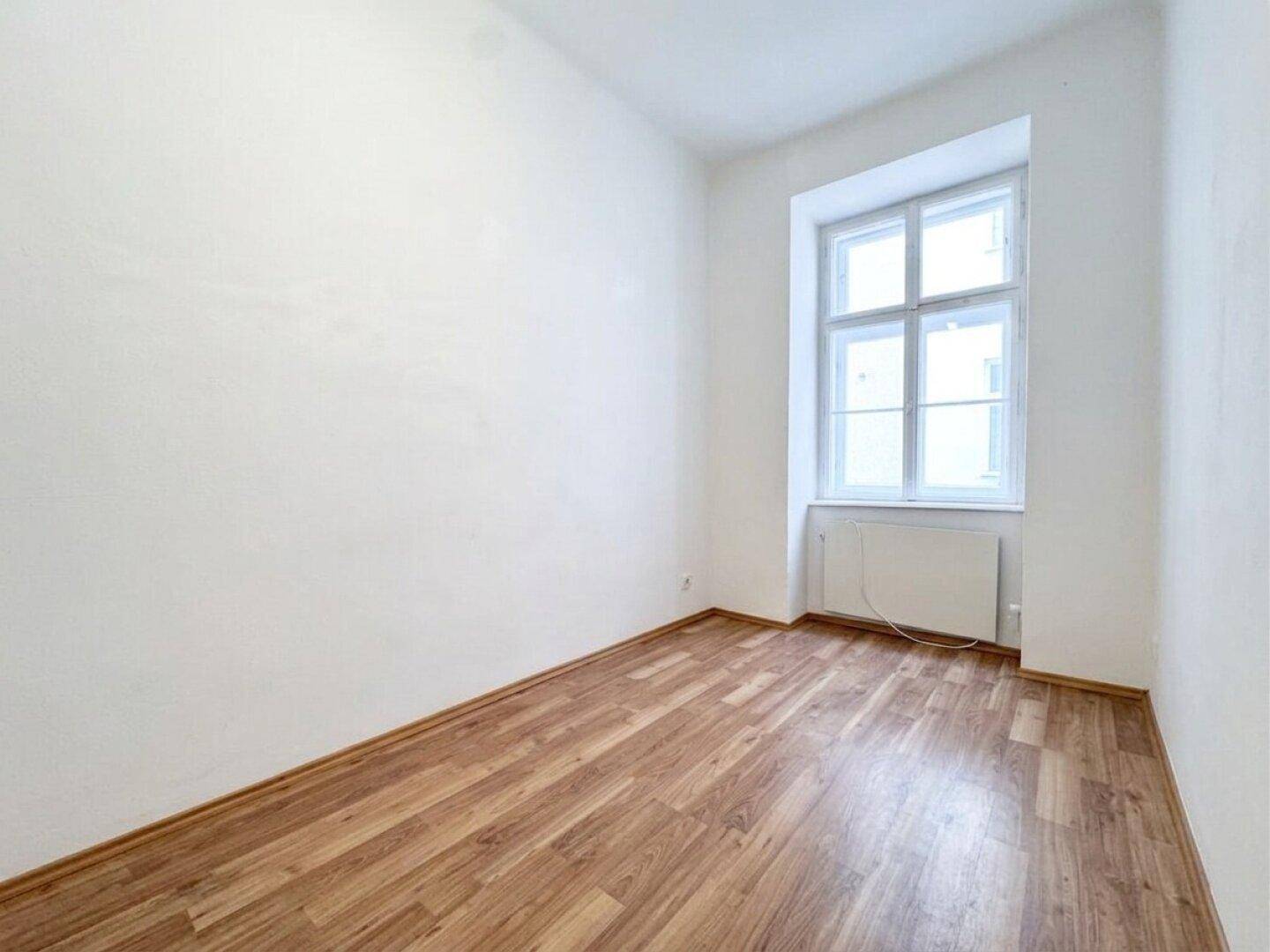 Heller, leerer Raum mit Laminatboden und großem Fenster, ideal für individuelle Gestaltung.