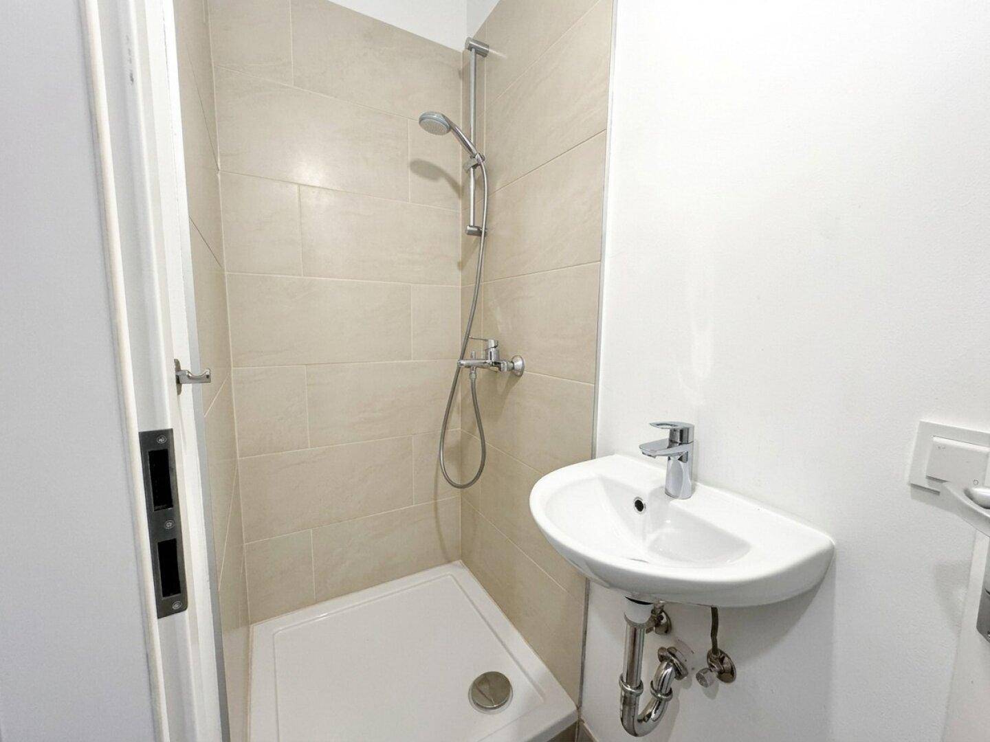 Modernes Badezimmer mit Duschkabine, Waschbecken und hellen Fliesen an den Wänden.