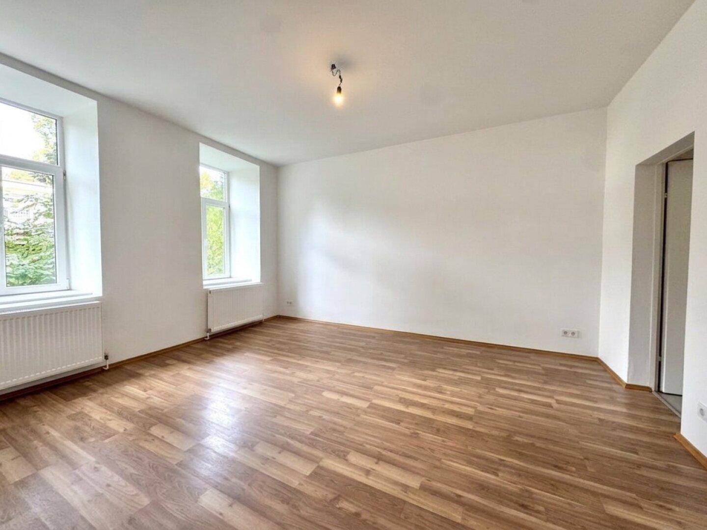 Leeres Wohnzimmer mit hellem Holzboden und weißen Wänden, bereit für individuelle Gestaltung.
