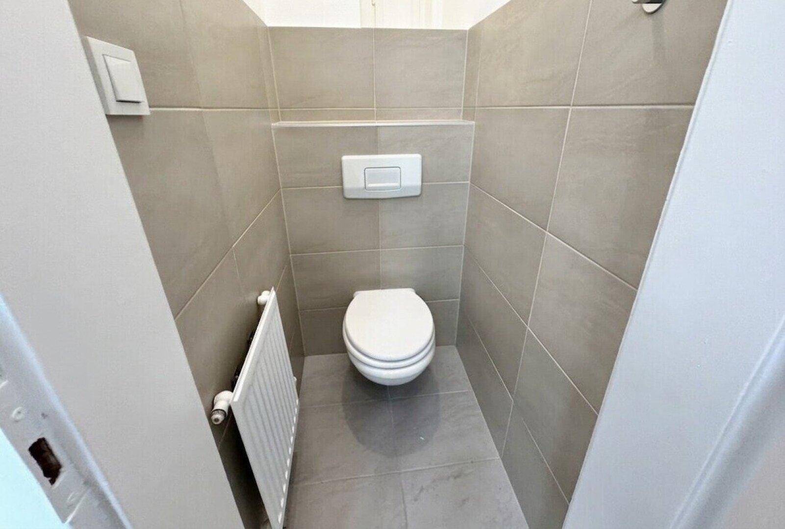 Modernes Gäste-WC mit beigefarbenen Fliesen, wandhängendem WC und Heizkörper.
