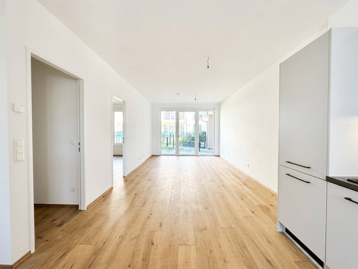 Heller, leerer Wohnbereich mit Eichenparkettboden und Zugang zur Terrasse oder Garten.