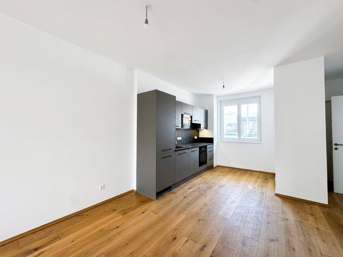 Moderne Einbauküche in Grau mit Holzparkettboden in einem hellen, offenen Raum.