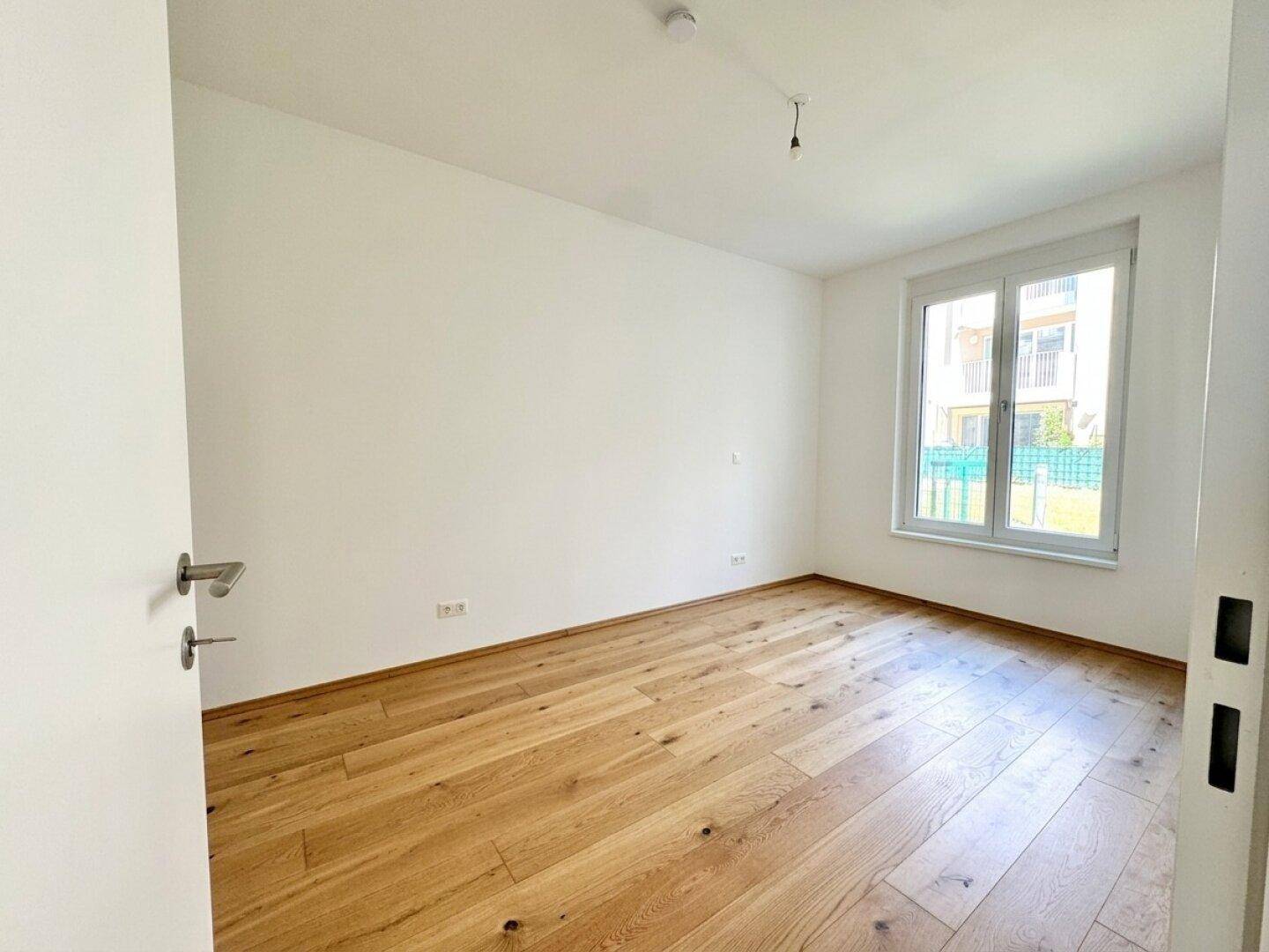 Helles Schlafzimmer mit Eichenparkettboden und großem Fenster mit Blick ins Grüne.