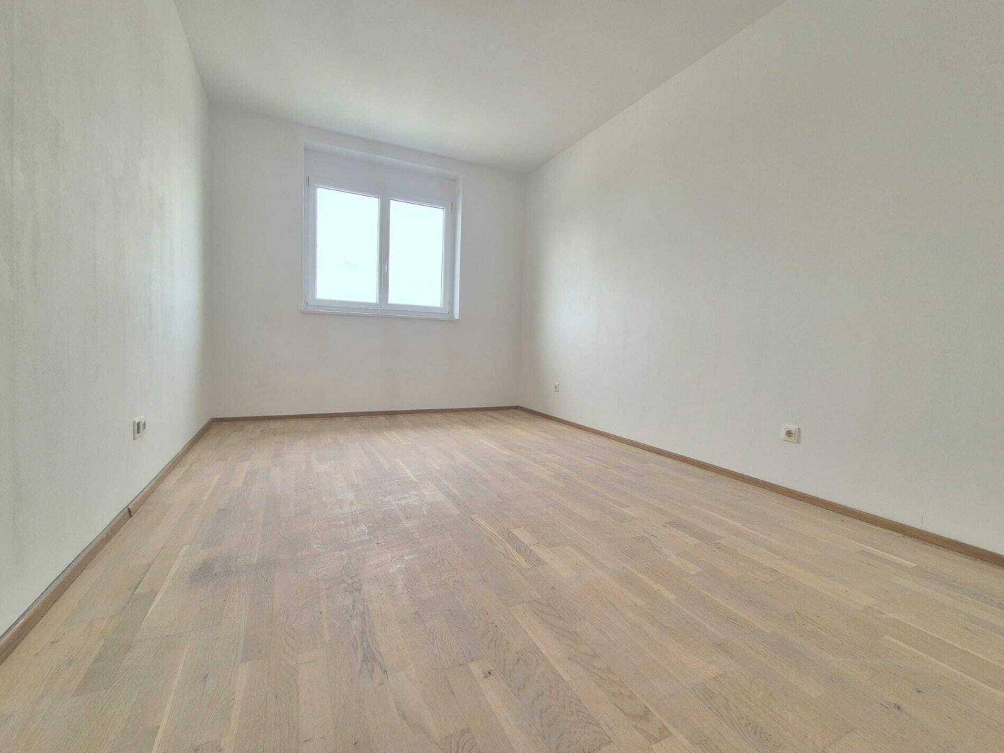 Heller, leerer Raum mit modernem Holzparkett und weiß gestrichenen Wänden.