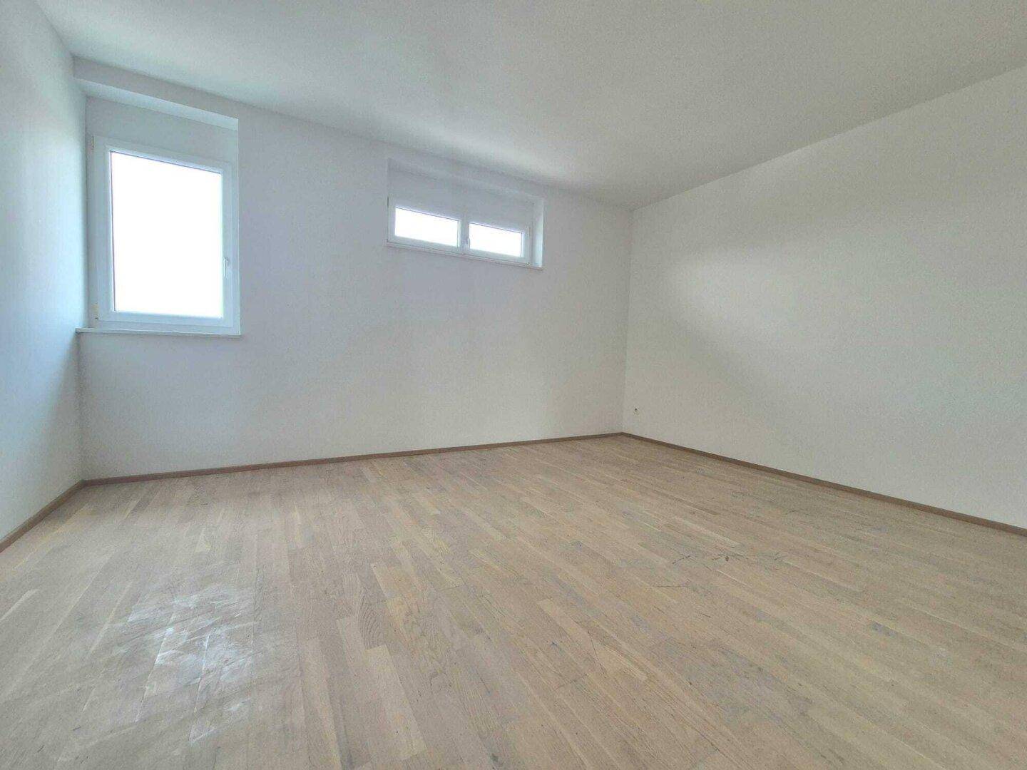Geräumiger, heller Raum mit zwei Fenstern und neuwertigem Holzfußboden.