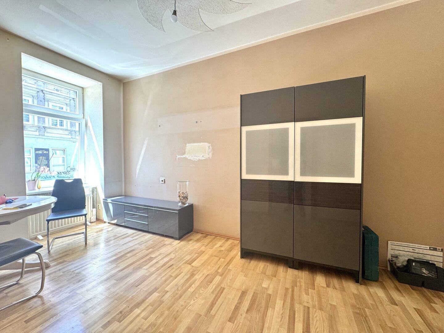 Geräumiges Wohnzimmer mit Parkettboden, großem Fenster und moderner Schrankwand.