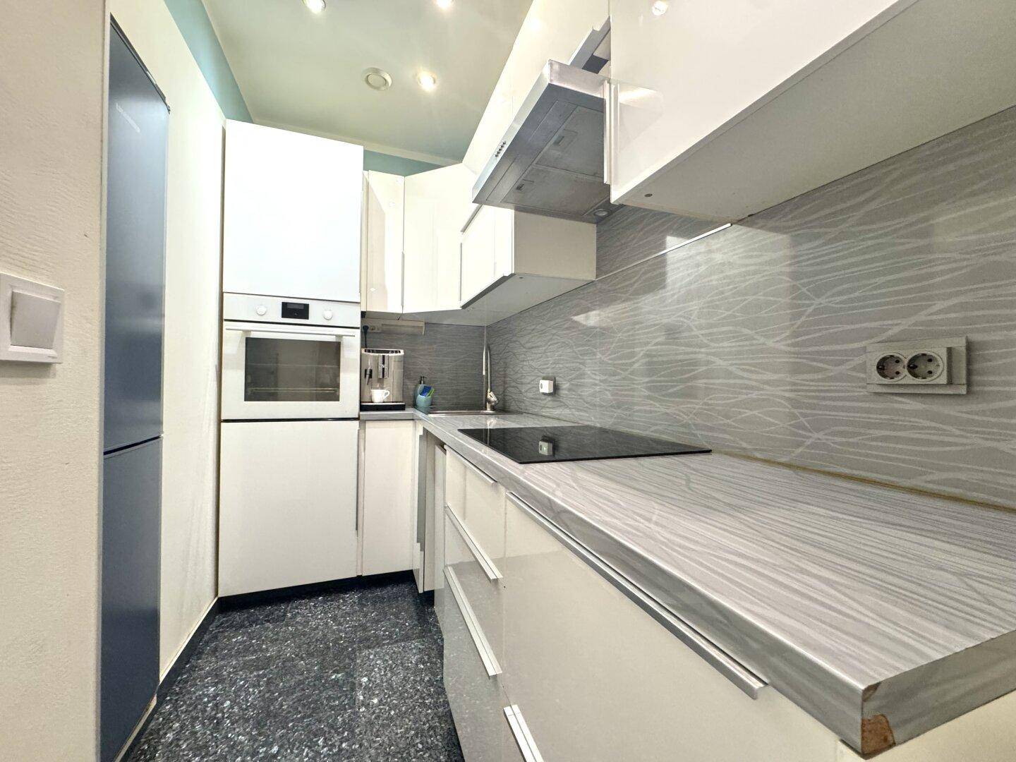 Moderne Einbauküche mit weißen Hochglanzfronten, Induktionskochfeld und integriertem Backofen.