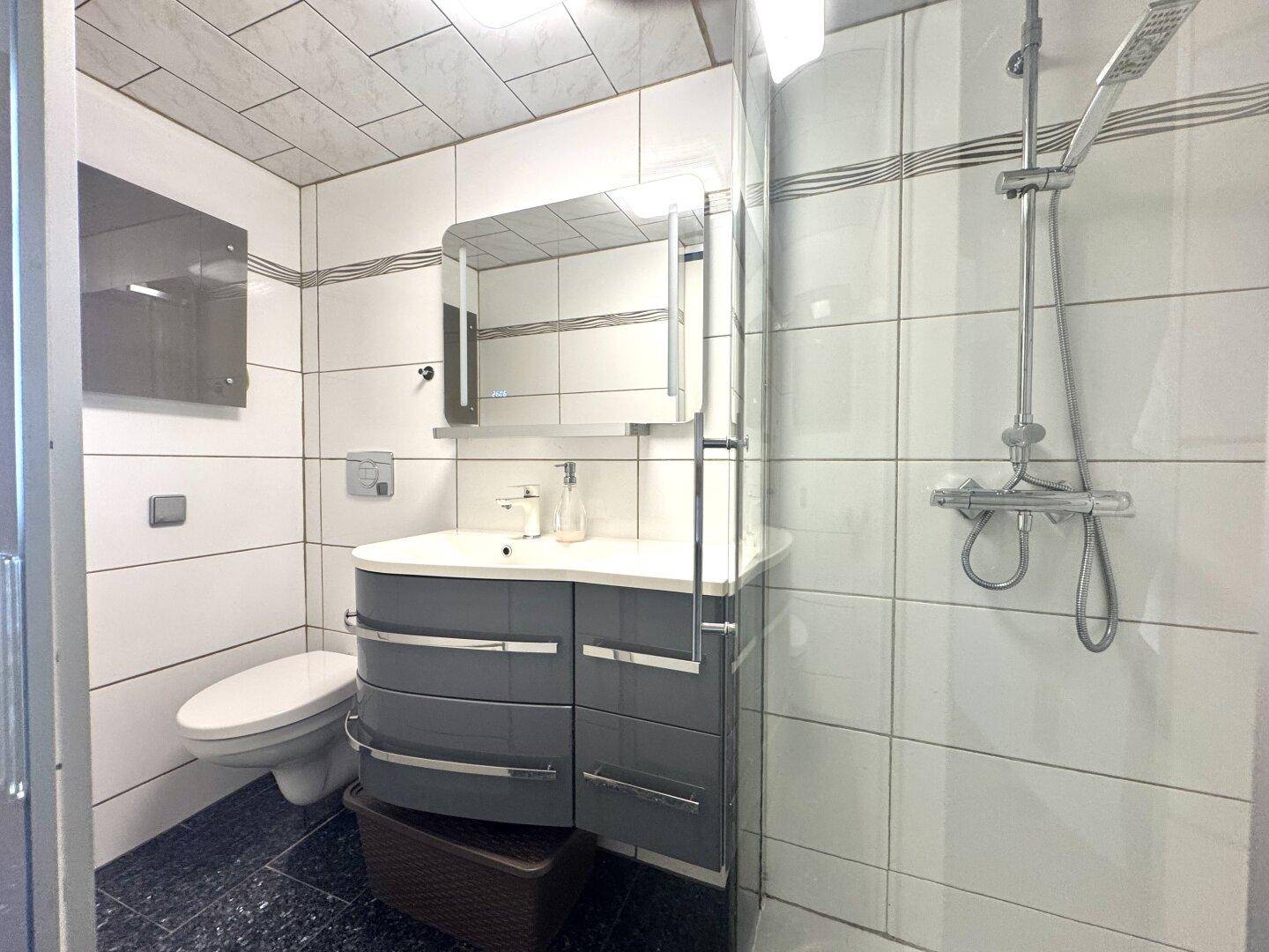 Modernes Badezimmer mit Dusche, Waschtischunterschrank und weißen Fliesen.