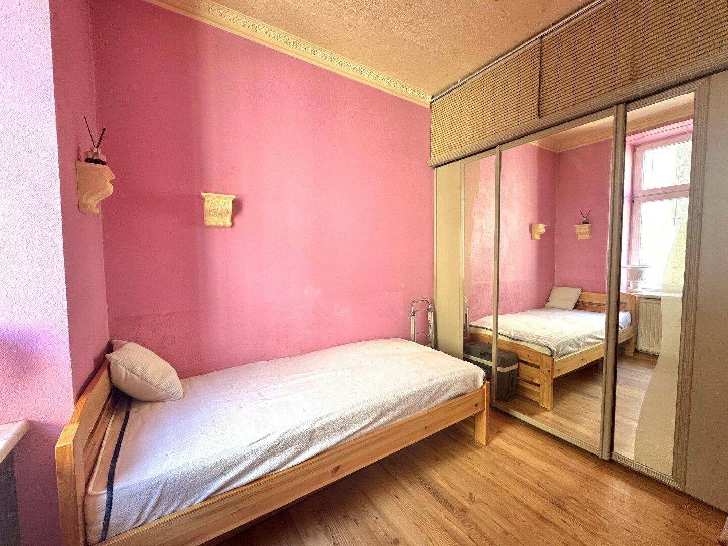 Gemütliches Schlafzimmer mit Holzbett, Spiegelschrank und rosa gestrichenen Wänden.