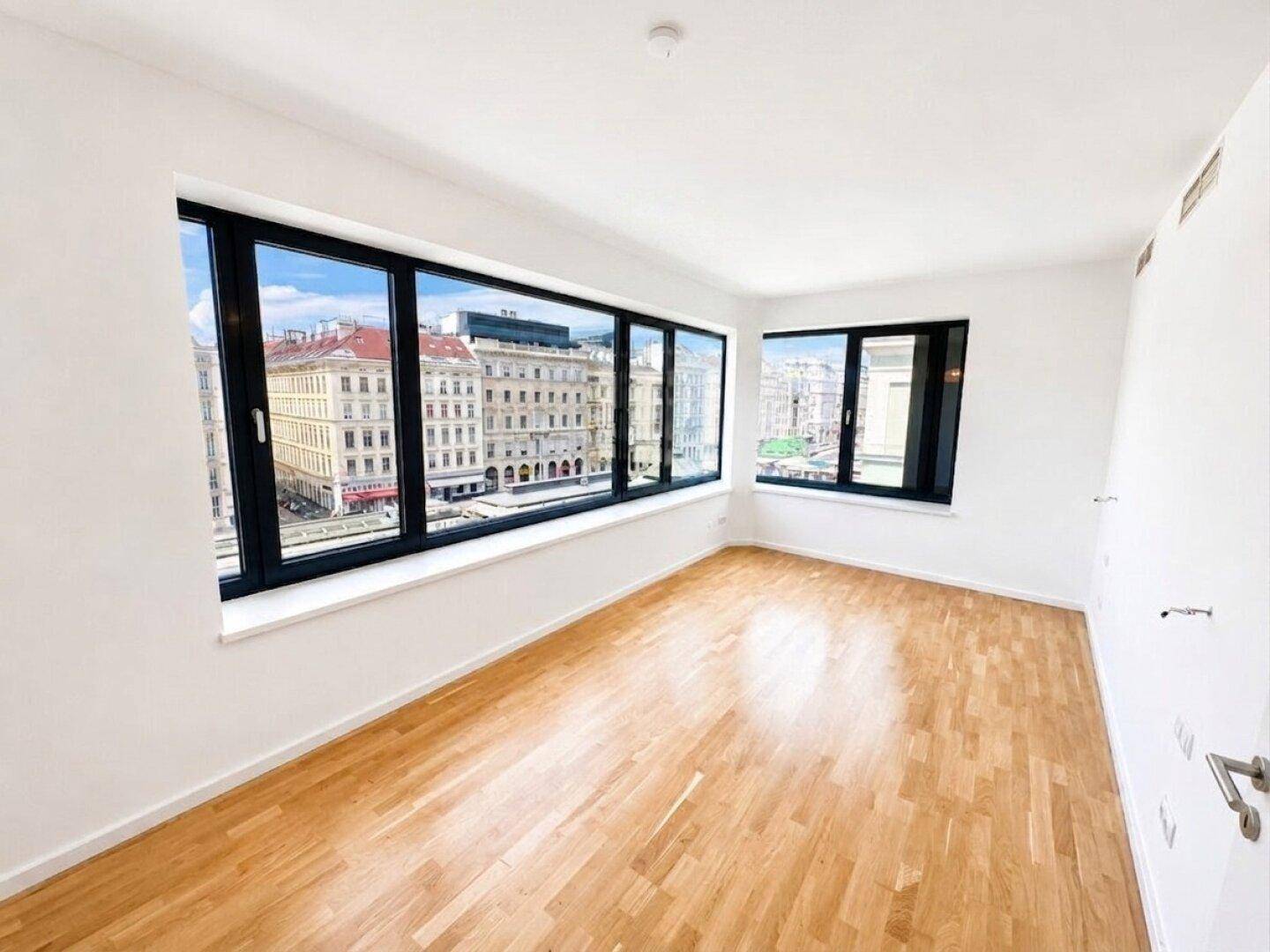 Helles Zimmer mit Holzboden und großen Fenstern, die einen weiten Blick auf die Stadt bieten.
