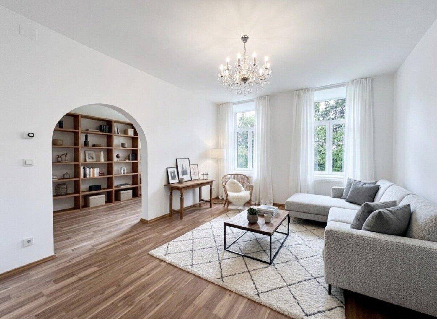 Geschmackvoll eingerichtetes Wohnzimmer mit Kronleuchter, Holzboden und einem Bogen zu Einbauregalen.