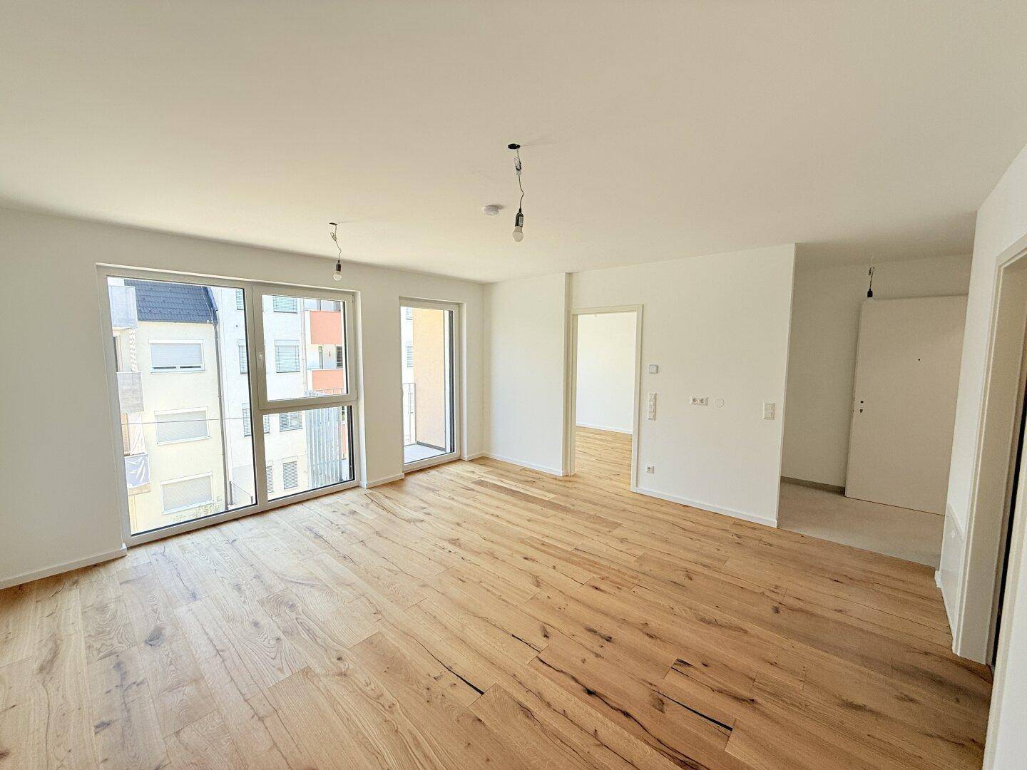Lichtdurchflutetes Wohnzimmer mit Holzboden und Zugang zu einem Balkon, bereit für die Einrichtung.