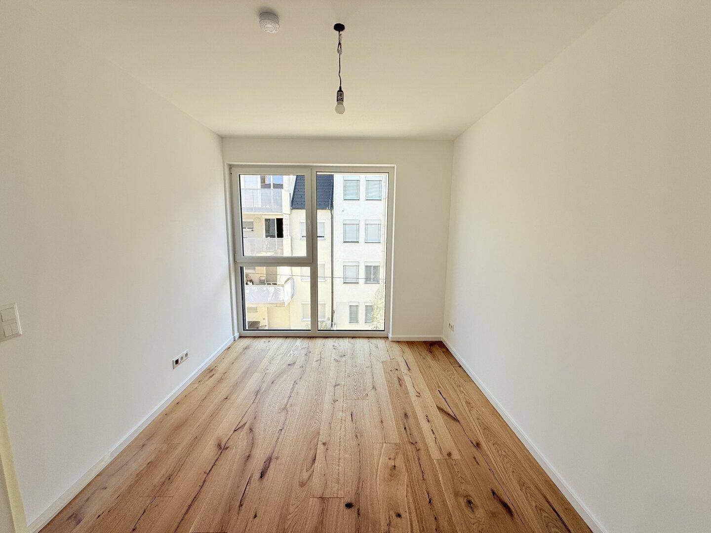 Helles Schlafzimmer mit Holzboden und Blick auf die umliegenden Gebäude, ideal für Ruhe.