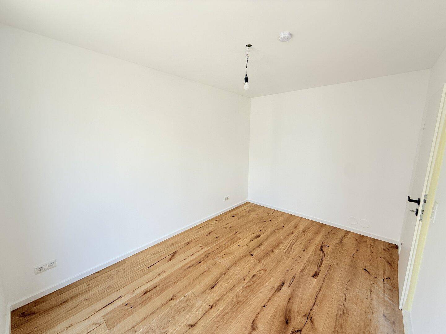 Gemütliches Schlafzimmer mit Holzboden und weißen Wänden, bereit für individuelle Gestaltung.
