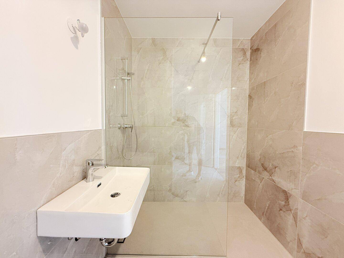 Elegantes Badezimmer mit großzügiger begehbarer Dusche und modernem Waschbecken, in warmen Beigetönen.