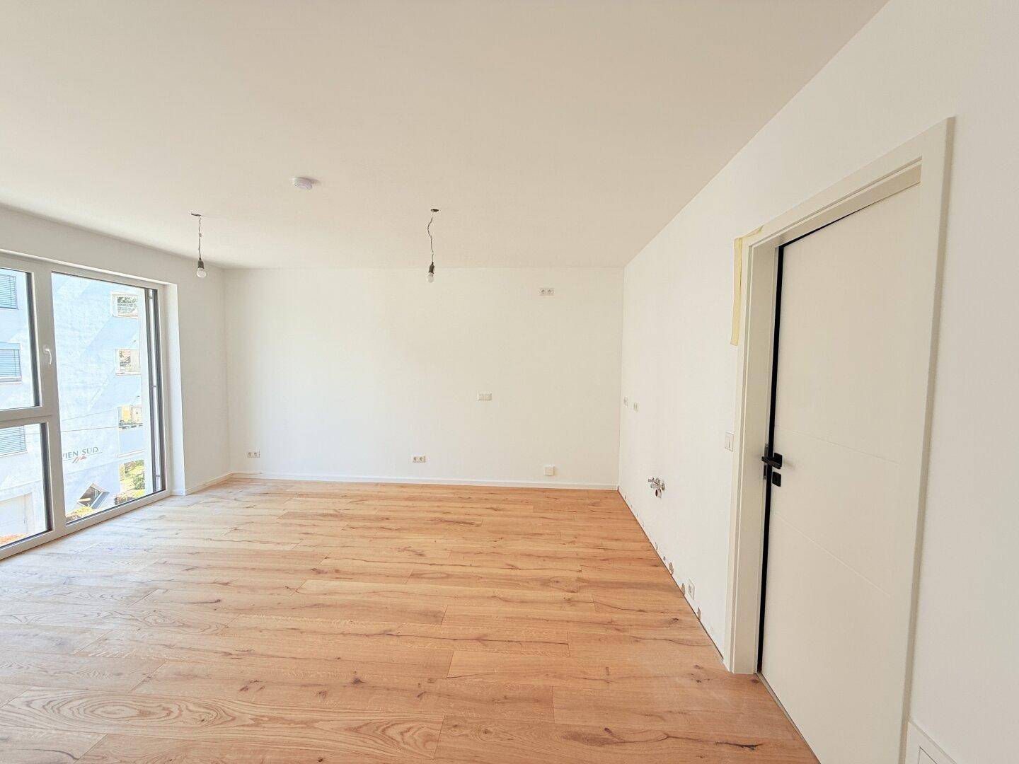Geräumiges, unmöbliertes Wohnzimmer mit großen Fenstern und hellem Holzboden, ideal für neue Bewohner.