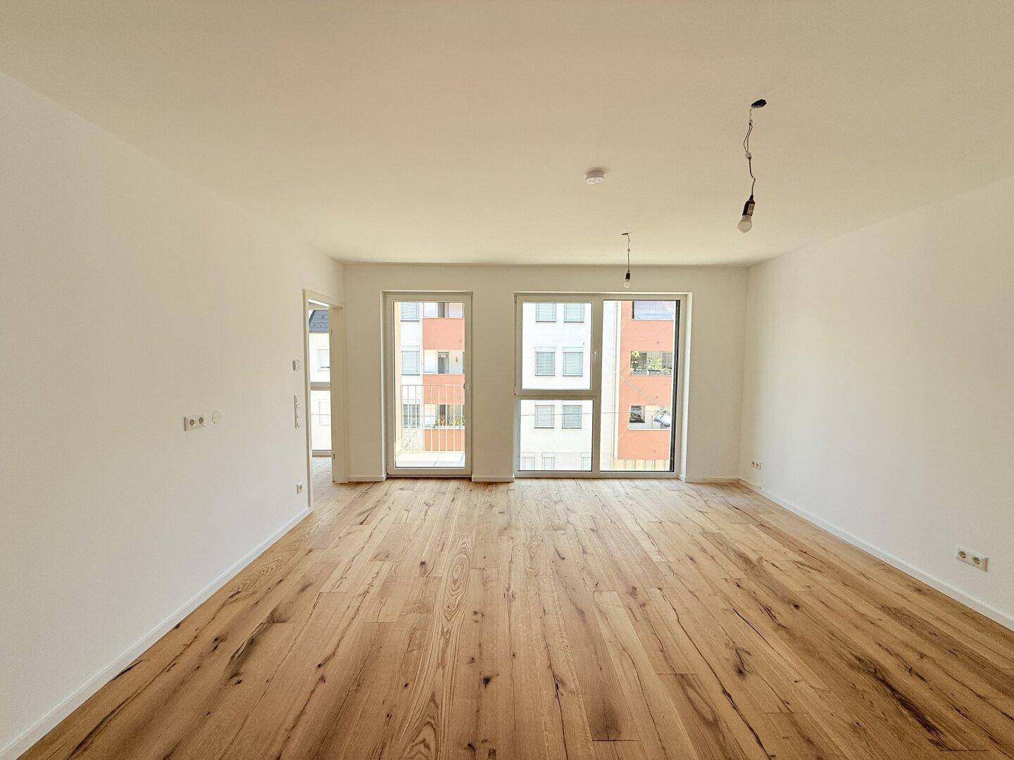 Lichtdurchfluteter Wohnbereich mit Eichenparkett und zwei Fenstertüren, die viel Tageslicht hereinlassen.