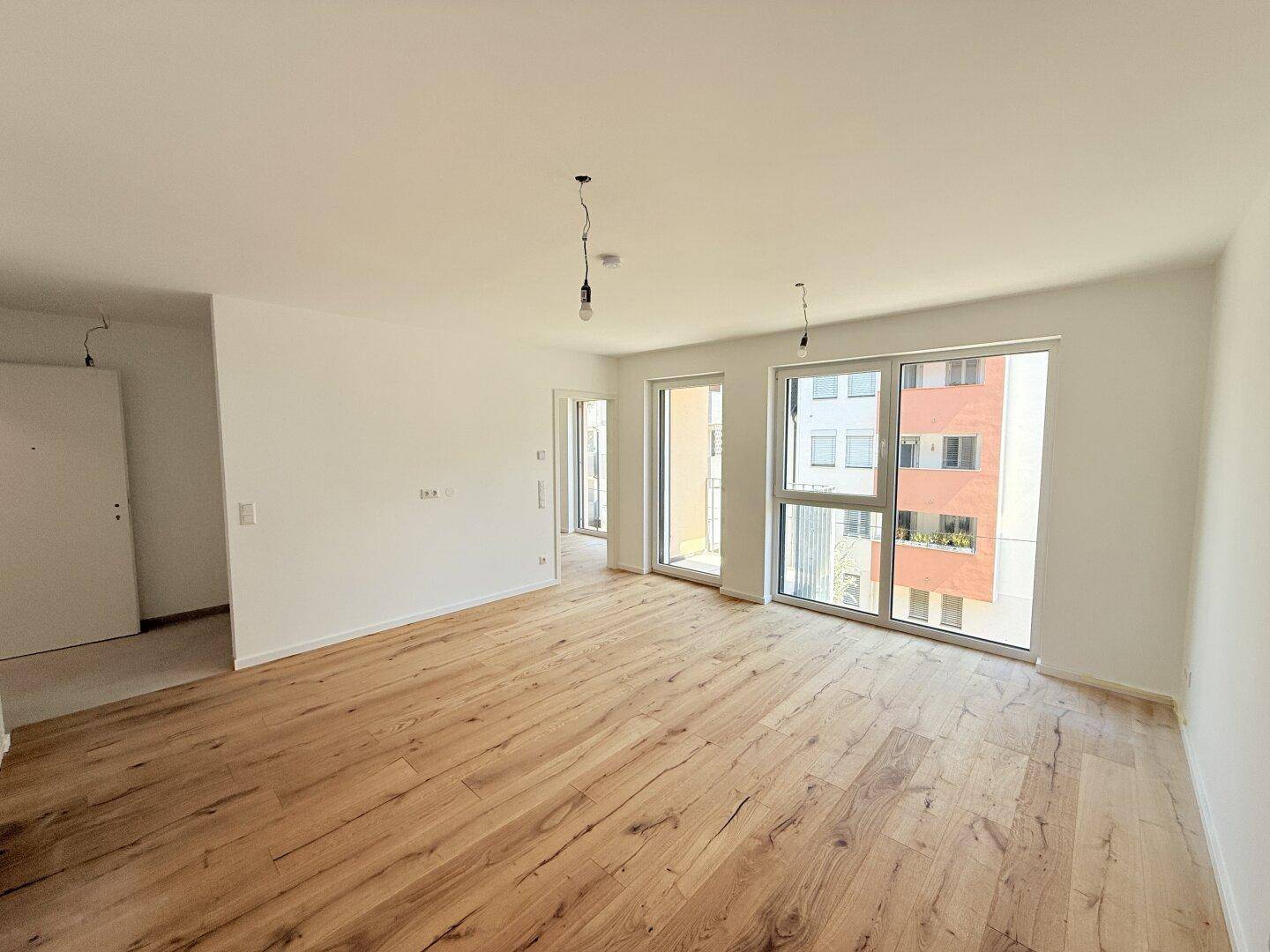Heller Wohnraum mit neuem Holzboden und großen Fenstern, die einen Blick auf die Umgebung bieten.