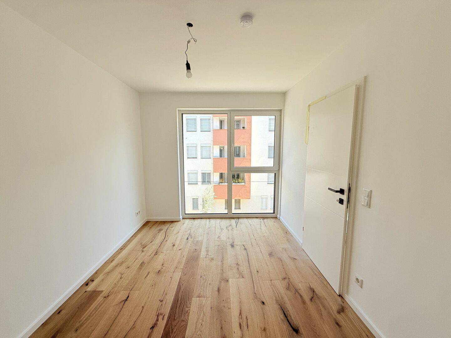 Unmöbliertes Zimmer mit Holzboden und Fenstertür, die einen Zugang nach draußen ermöglicht.
