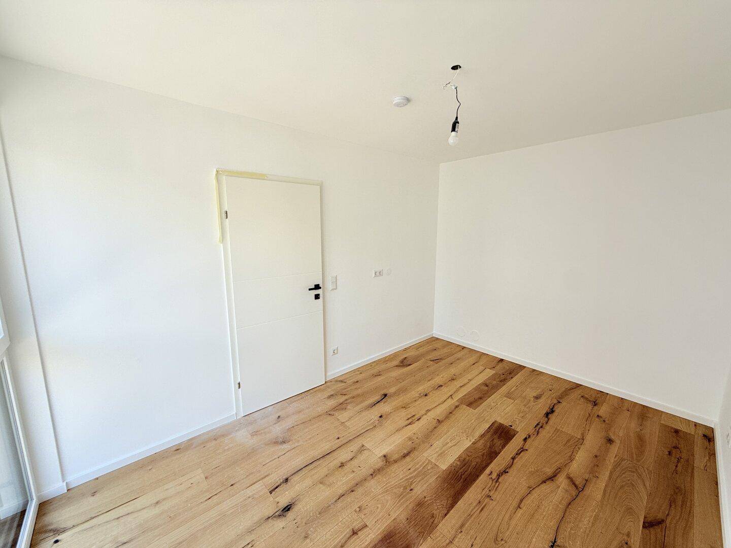 Helles Zimmer mit Holzboden und weiß gestrichenen Wänden, bereit für die Einrichtung.