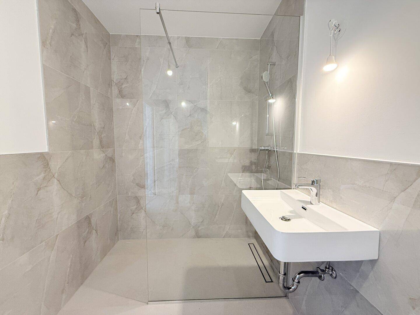 Modernes Badezimmer mit großformatigen Fliesen, bodengleicher Dusche und minimalistischem Waschbecken.