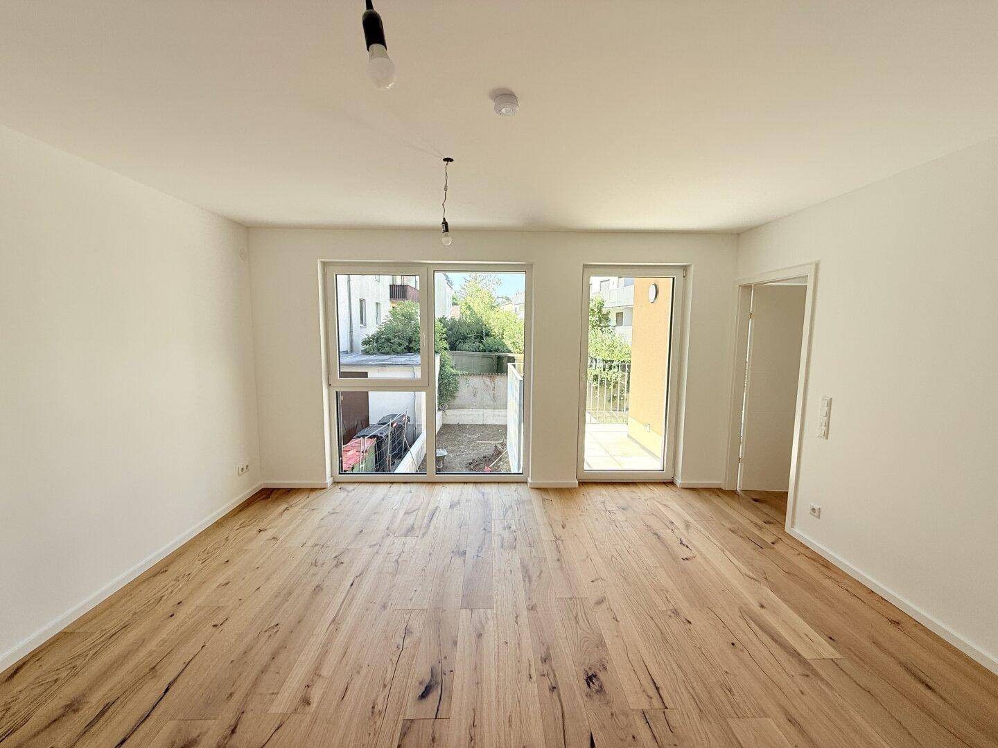 Geräumiges, helles Zimmer mit Holzboden und großen Fenstern, die viel Tageslicht hereinlassen.