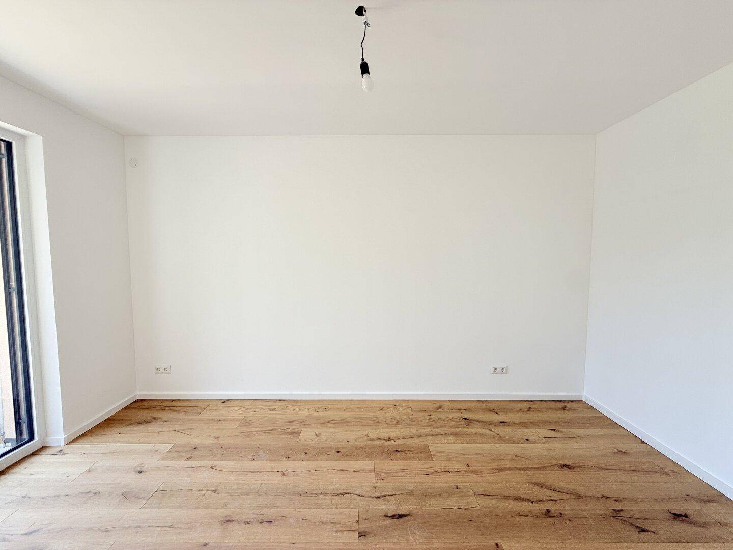 Leeres Zimmer mit Holzboden und weiß gestrichenen Wänden, bereit zur Einrichtung.
