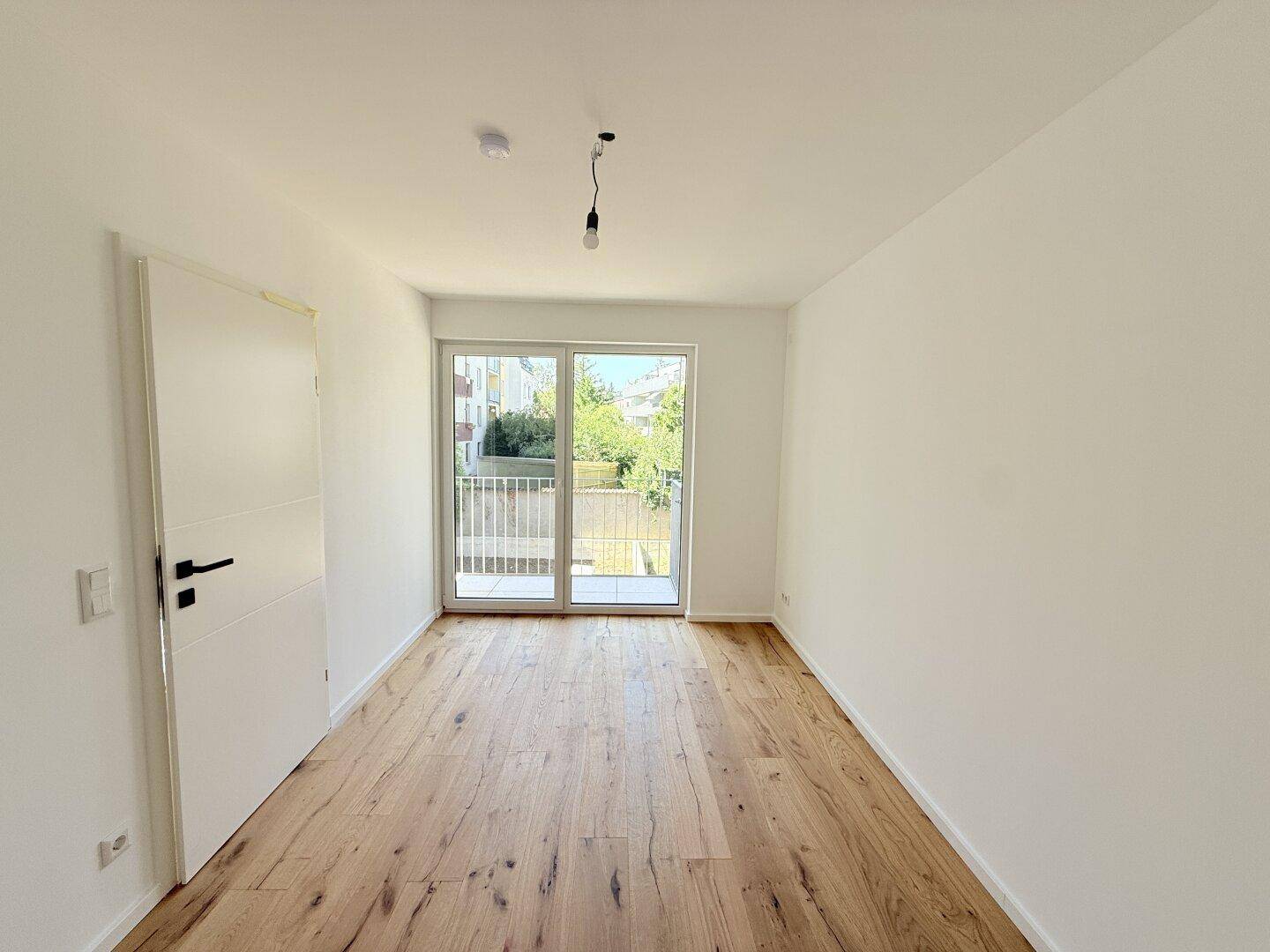 Helles Zimmer mit Holzboden und Zugang zu einem Balkon, ideal als Schlafzimmer nutzbar.