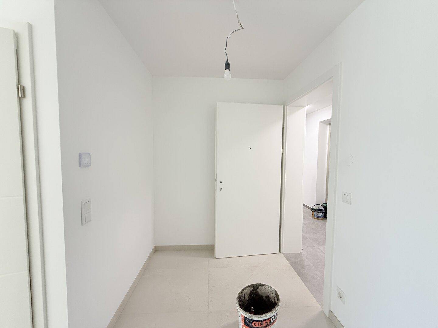 Heller Flur mit Fliesenboden und weißer Tür, der zu weiteren Räumen der Wohnung führt.