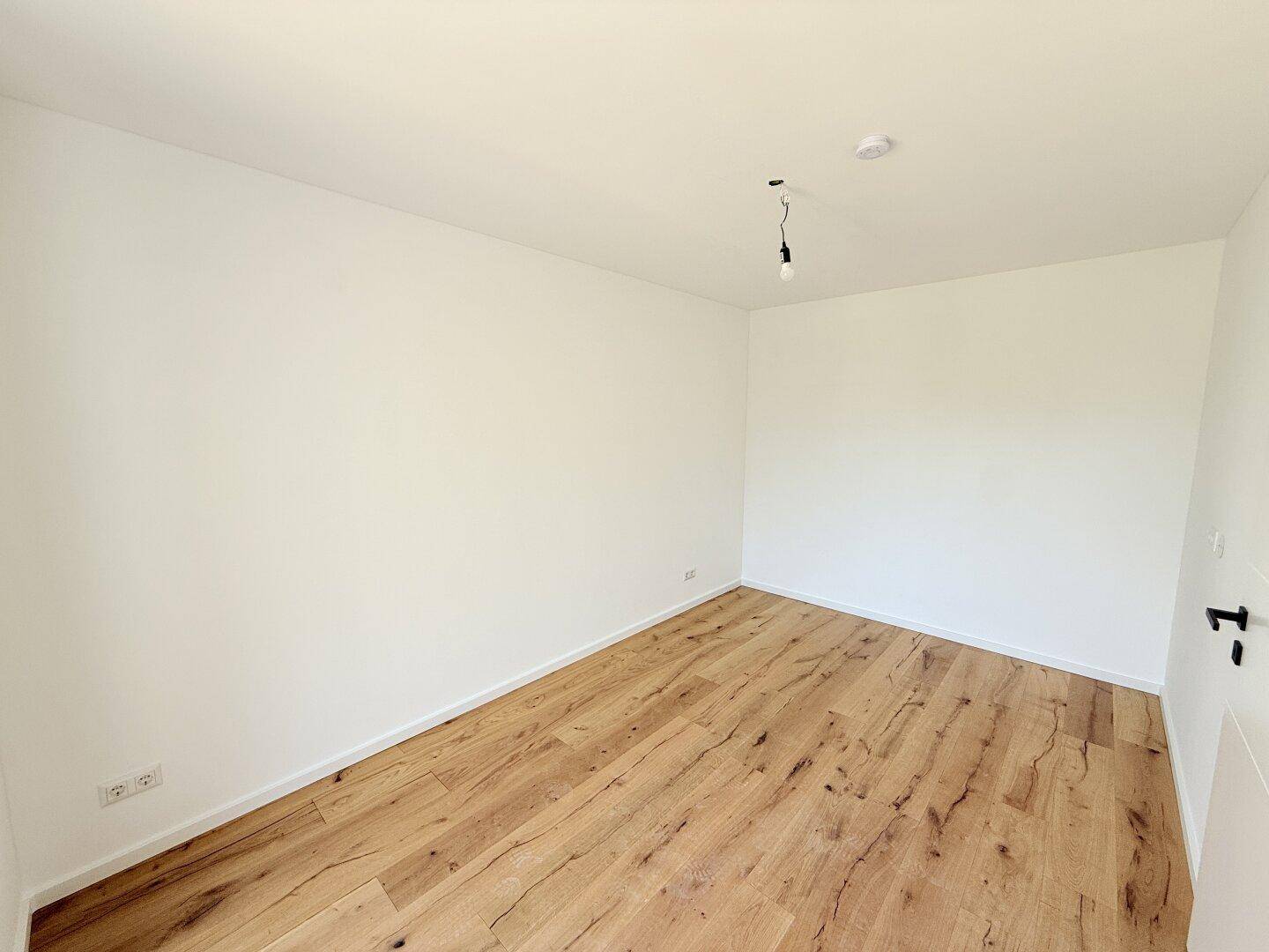 Unmöblierter Raum mit Holzboden und weißen Wänden, ideal für ein Schlafzimmer oder ein Arbeitszimmer.