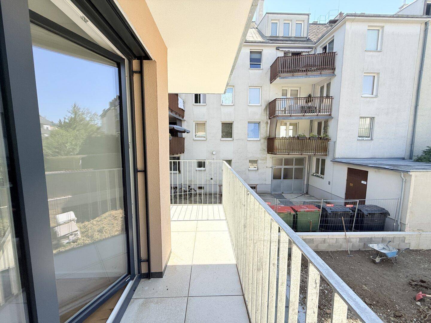 Balkon mit Metallgeländer und Blick auf den Innenhofbereich mit Mülltonnen und angrenzenden Gebäuden.