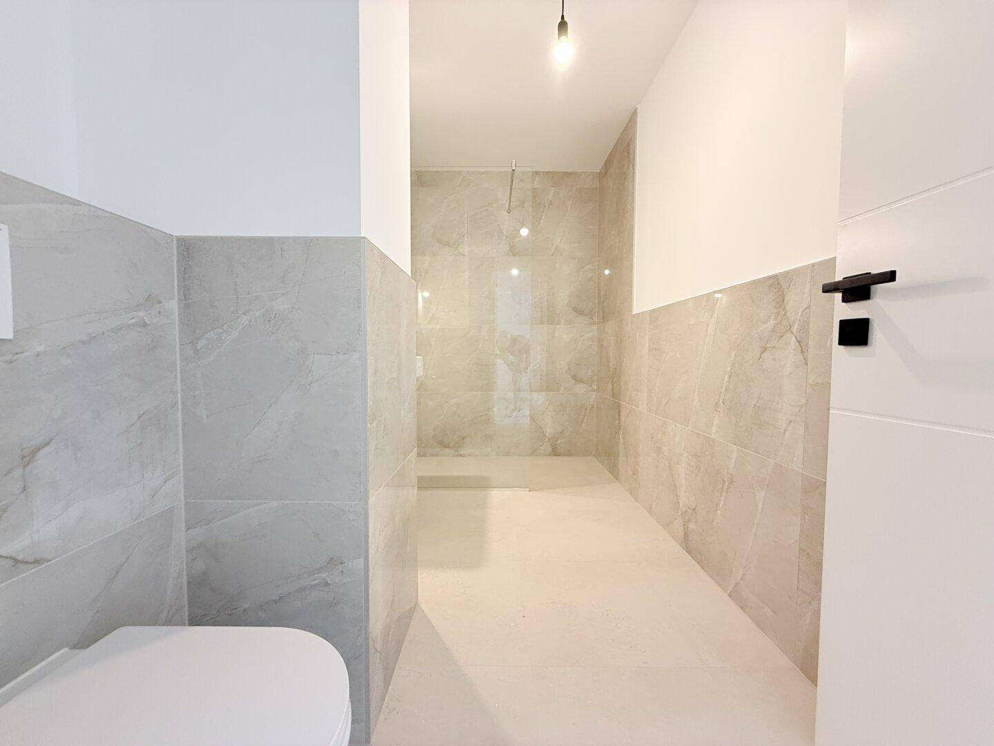 Modernes Badezimmer mit grauen Fliesen und einer geräumigen, ebenerdigen Dusche, sehr gepflegt.
