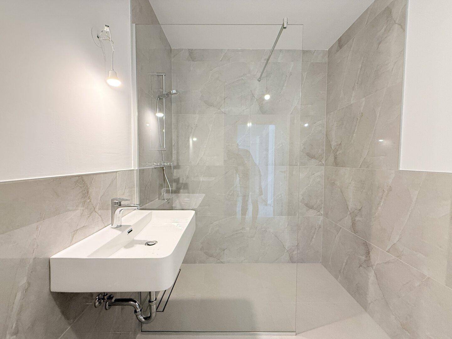 Modernes Badezimmer mit Waschbecken, großer Dusche und hellgrauen Fliesen, bietet viel Komfort.