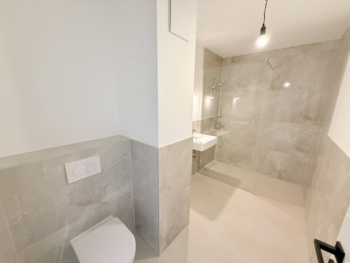 Helles Badezimmer mit modernen Fliesen, wandhängendem WC und ebenerdiger Dusche, sehr funktional.