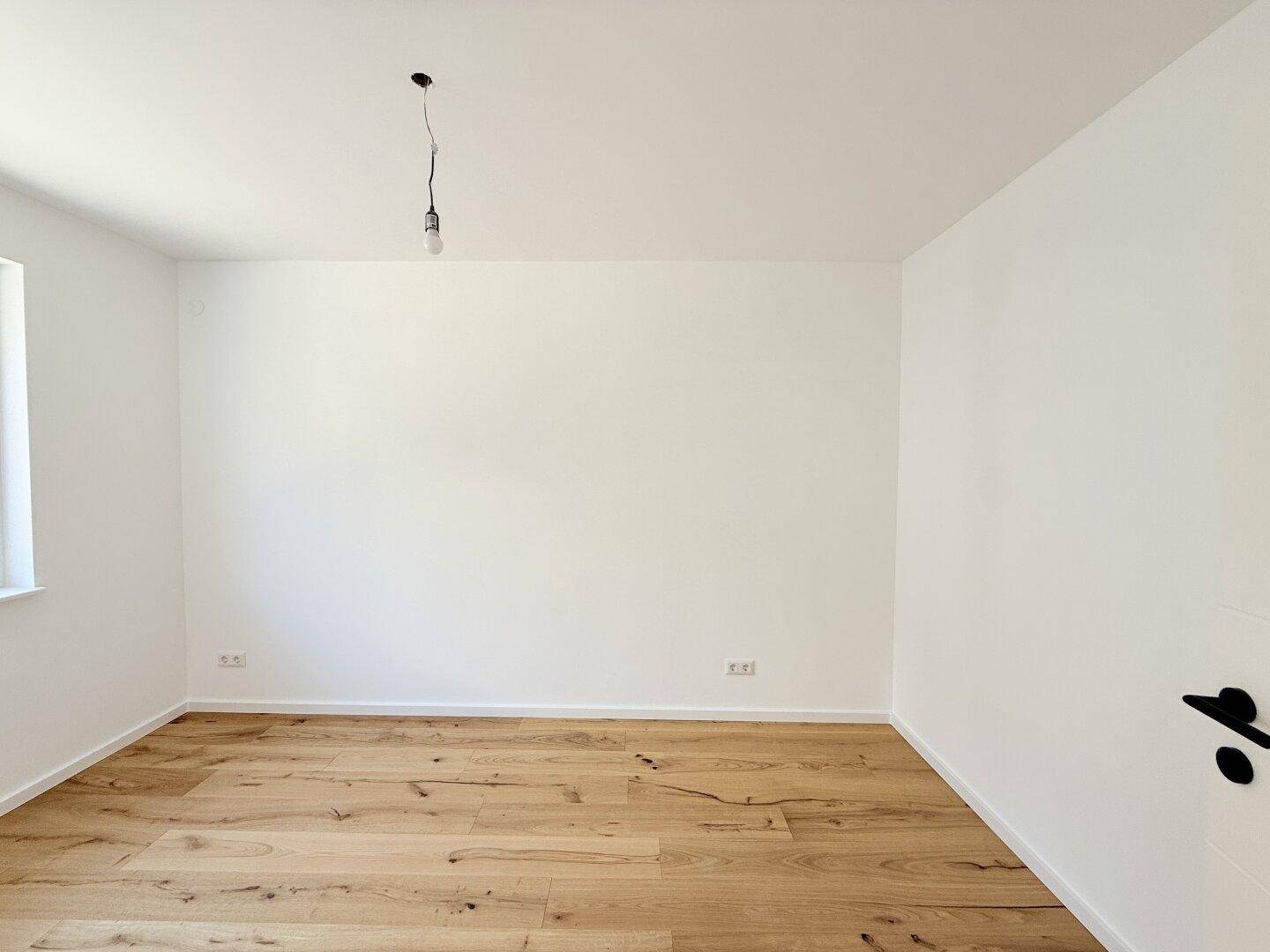 Heller, leerer Raum mit weißen Wänden und neuem Holzfußboden, bereit zum Einzug.