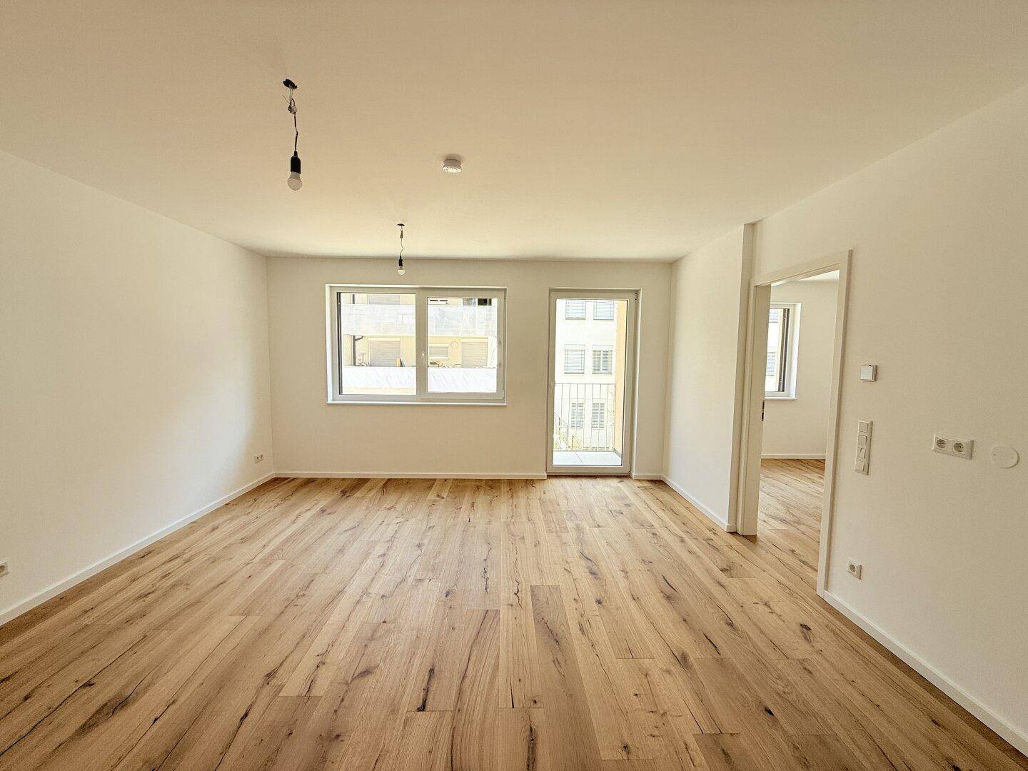 Geräumiges, helles Zimmer mit Holzboden, Zugang zu einem Balkon und Blick auf die Umgebung.
