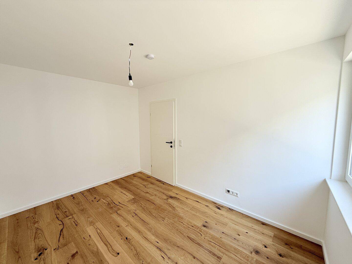 Helles Schlafzimmer mit Holzboden und weiß gestrichenen Wänden, bereit für die Einrichtung.