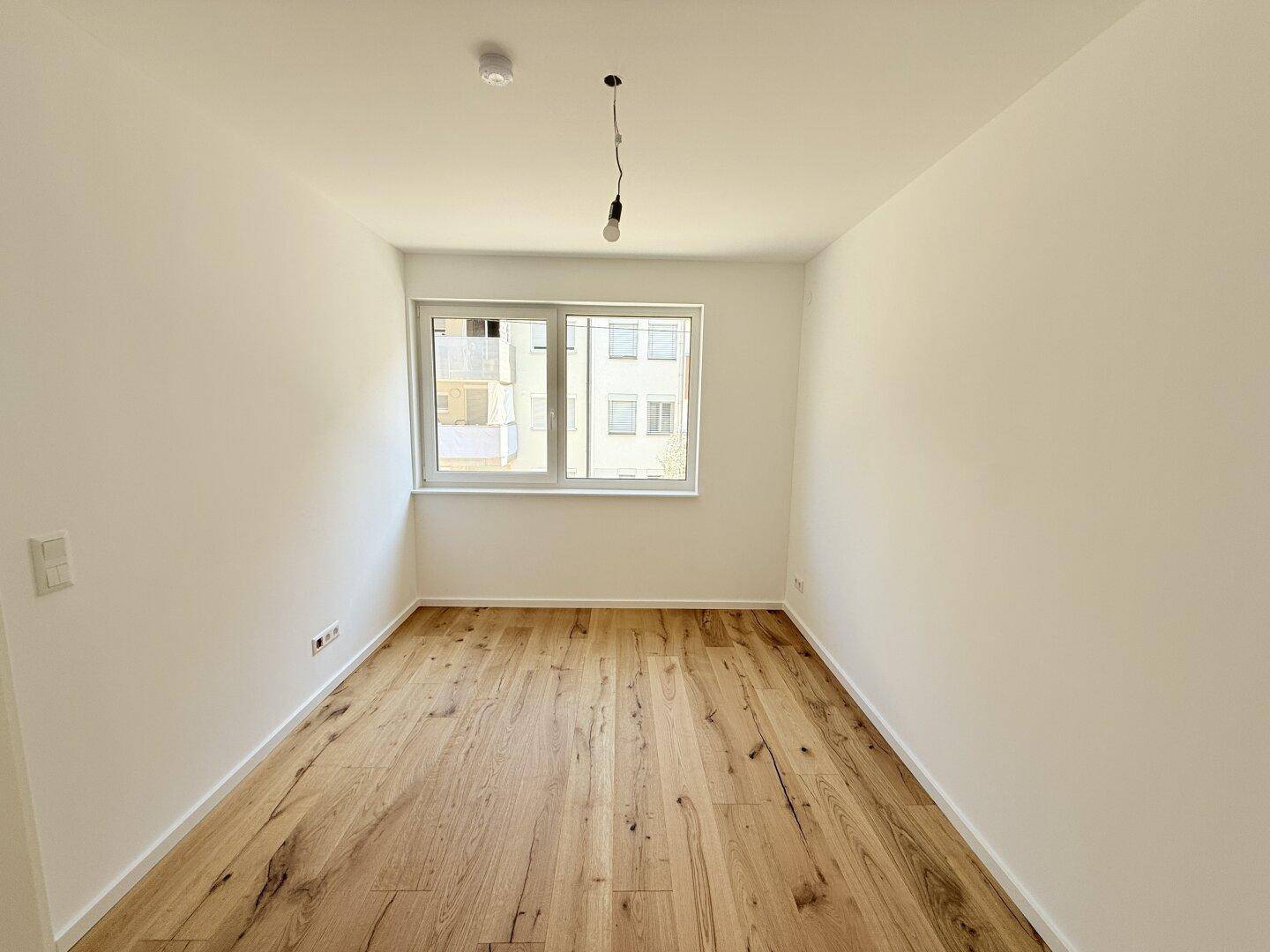 Gemütliches Zimmer mit Holzboden und großem Fenster, bietet viel Tageslicht und eine angenehme Atmosphäre.