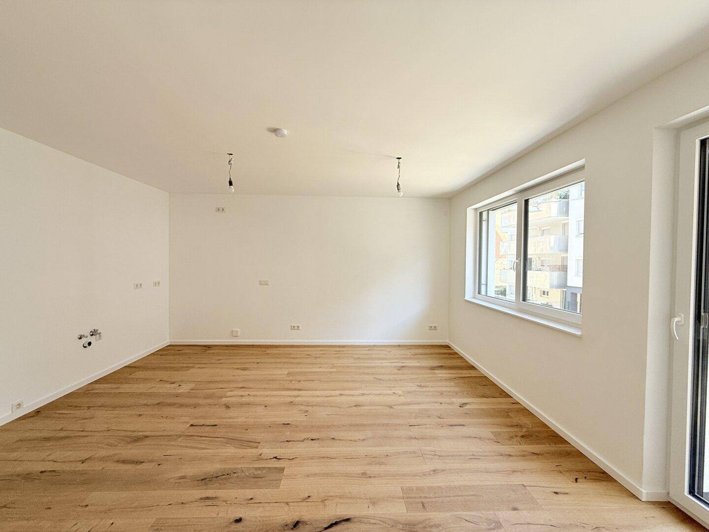 Lichtdurchfluteter Raum mit modernem Holzboden und großen Fenstern, ideal für Wohnzwecke.